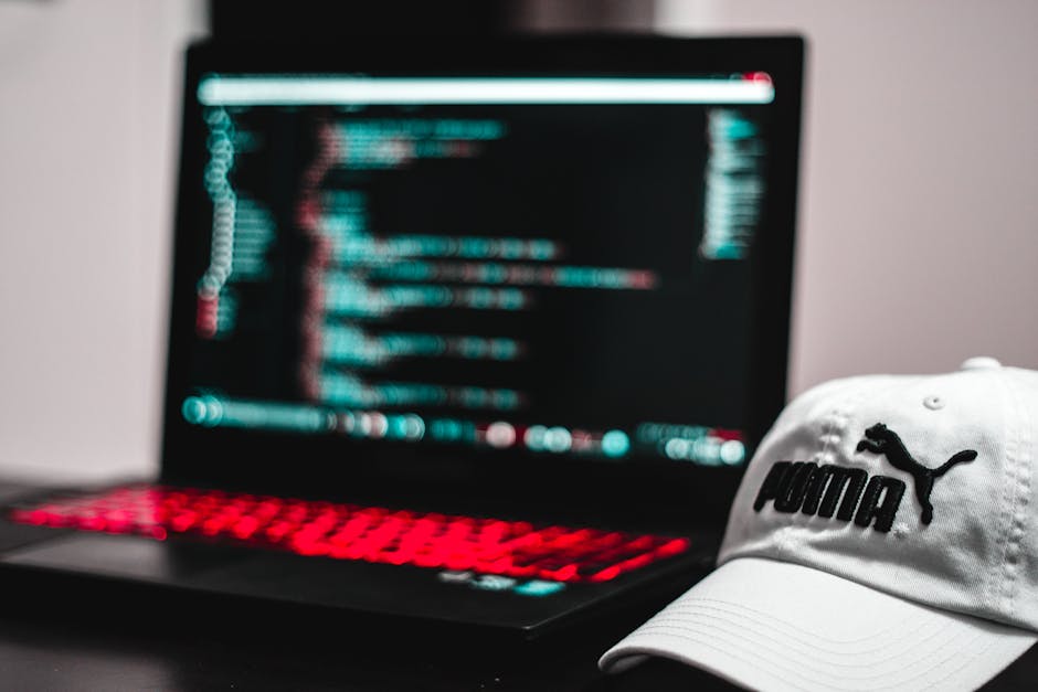 A person’s hands are positioned over a laptop keyboard, with the left hand resting on the left side and the right hand on the right side of the device. The laptop screen displays a dark-themed code 